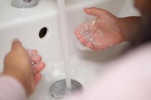 ragazzo fabbricazione un' detergente gesto con sapone e acqua su mani foto