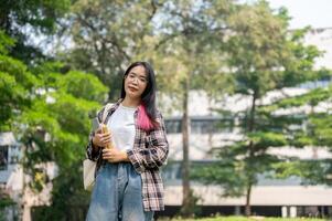 un' fiducioso giovane asiatico femmina Università alunno è guardare a il telecamera mentre in piedi nel il parco. foto