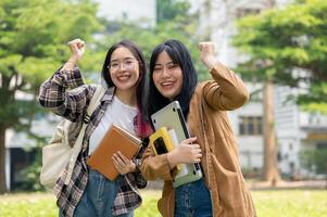 Due eccitato asiatico femmina studenti siamo raccolta loro pugni nel celebrazione mentre in piedi all'aperto. foto