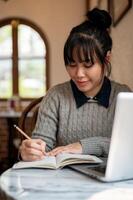 un' femmina Università alunno nel casuale indossare è lettura un' manuale o fare compiti a casa nel un' bar. foto