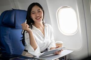 un' fiducioso asiatico donna d'affari è seduta a un' finestra posto a sedere su un' aereo con sua digitale tavoletta. foto