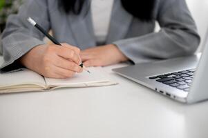 un' ritagliata tiro di un' donna d'affari focalizzata su scrittura o assunzione Appunti nel il taccuino con un' matita. foto