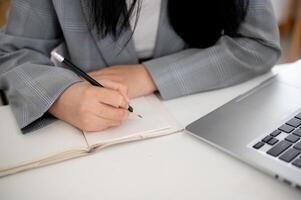 un' ritagliata tiro di un' donna d'affari focalizzata su scrittura o assunzione Appunti nel il taccuino con un' matita. foto