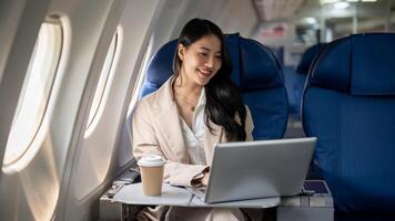 un attraente asiatico femmina Amministratore delegato è Lavorando su sua il computer portatile durante il volo per sua attività commerciale viaggio. foto