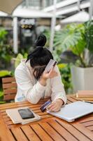 un' irritato asiatico donna mano copertura sua viso mentre Tenere un' credito carta, avendo finanziario i problemi. foto