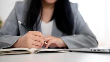 un' ritagliata tiro di un' donna d'affari focalizzata su scrittura o assunzione Appunti nel il taccuino con un' matita. foto