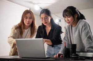 un' femmina fotografo è controllo immagini su sua il computer portatile e Lavorando nel il studio con sua assistenti foto