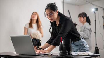 un' fiducioso femmina fotografo controllo immagini su sua computer portatile, Lavorando con sua squadra nel il studio. foto