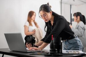 un' fiducioso femmina fotografo controllo immagini su sua computer portatile, Lavorando con sua squadra nel il studio. foto