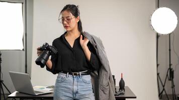 un' fiducioso asiatico femmina fotografo è in piedi nel sua studio con un' dslr telecamera nel sua mano. foto