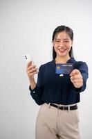 un attraente asiatico donna è mostrando un' credito carta per il telecamera, studio sfondo. in linea pagamento foto