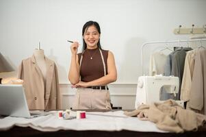 un attraente asiatico femmina moda progettista o sarto è nel sua studio, sorridente a il telecamera. foto