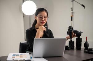 un' professionale asiatico femmina fotografo è messa a fuoco su controllo immagini su sua il computer portatile. foto