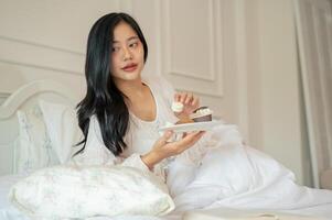 un attraente asiatico donna nel lungo vestito pigiama è avendo prima colazione nel letto. foto