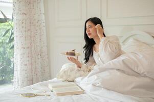 un attraente asiatico donna nel lungo vestito pigiama è avendo prima colazione nel letto. foto