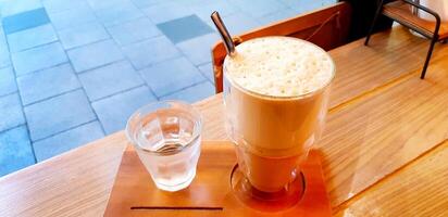 caramello macchiato frappé con ghiacciato acqua su il di legno tavolo con copia spazio a bar negozio. rinfresco potabile concetto foto