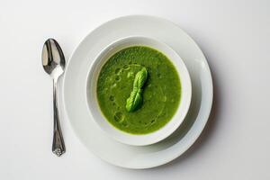 ciotola di verde piselli crema la minestra la minestra, con basilico foglie, oliva olio su un' bianca piatto, piatto con un' cucchiaio. bianca tavolo su sfondo foto