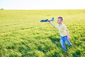 ragazzo corre con giocattolo aereo nel estate attraverso campo. contento bambino in esecuzione e giocando con giocattolo aereo all'aperto. ragazzo sogni di volare. spensierato bambino è giocando. foto