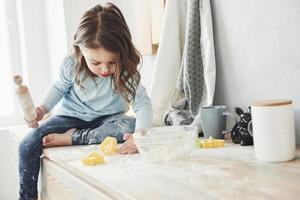 da solo nella stanza quando i genitori non sono a casa. foto di una bambina carina che si siede sul tavolo della cucina e gioca con la farina