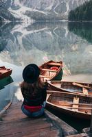 scala nell'acqua. donna con cappello nero che si gode un maestoso paesaggio di montagna vicino al lago con barche foto