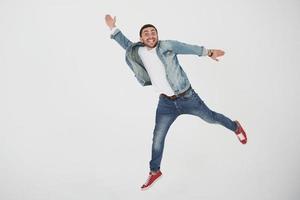 l'immagine di un giovane allegro vestito casual che salta su uno sfondo bianco fa un gesto diverso foto