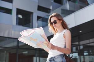 turista femminile con mappa che visita una nuova città e sta cercando un modo per raggiungere l'hotel foto