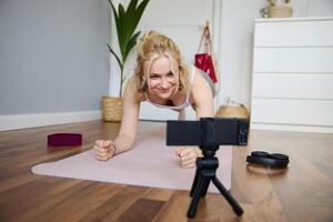ritratto di giovane sportivo vlogger, fitness istruttore in piedi nel tavola su gomma da cancellare yoga stuoia, registrazione di se stessa fare allenarsi a casa foto