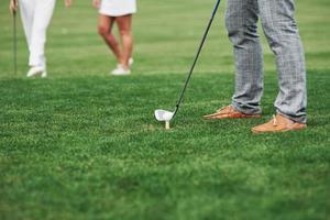 immagine ritagliata del giocatore di golf che prende di mira il tiro. due amici in piedi sullo sfondo foto