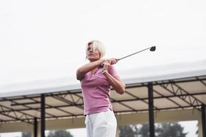 bionda donna adulta che segue la pallina da golf mentre tiene il bastone dopo un colpo foto