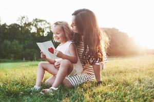 l'apprendimento è divertente. madre e figlia che si siedono e leggono il piccolo libro con il cuore sulla copertina foto