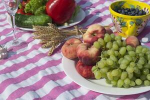 bellissimo picnic con frutta, verdure e bicchieri di vino vicino lago. foto