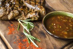 grigliato carne con salsa e rosmarino su un' di legno tavolo. foto