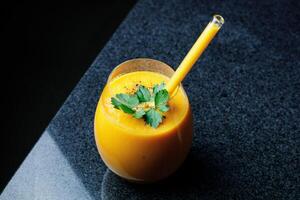 Mango carota Mela frullato nel un' bicchiere su buio sfondo con bicchiere cannuccia foto