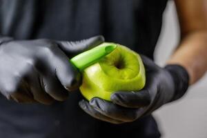 persona con nero guanti peeling un Mela con verde Mela pelapatate foto