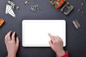 tavoletta modello su opera scrivania. del bambino mani toccare isolato Schermo. superiore Visualizza, piatto posare scrivania composizione con piccolo metallo parti e viti foto