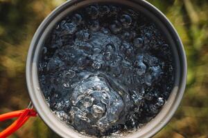 bollente acqua superiore Visualizza, turista utensili, riscaldamento acqua nel un' pentola, un' pentola per caldo bevande, aria bolle, spumeggiante liquido. foto