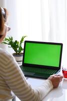 verticale indietro al di sopra di spalla Visualizza di anziano donna con bicchieri Guardando educativo seminario web, in linea conferenza seminario su il computer portatile con verde schermo, assunzione Appunti. il concetto di distanza formazione scolastica. foto