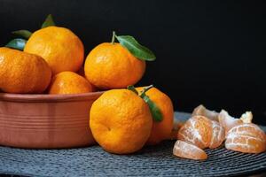 fresco maturo arancia mandarini, clementine, mandarini con le foglie nel un' ciotola su tavolo. pelato affettato frutta su grigio tovaglietta con nero sfondo. selettivo messa a fuoco. benefico proprietà per Salute. foto