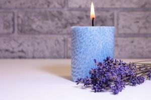 bouquet secco di fiori di lavanda vicino a una candela blu accesa sullo sfondo di un muro di mattoni sfocato all'interno. foto