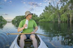 anziano maschio paddler nel un' addobbato spedizione canoa su un' calma lago nel settentrionale Colorado foto