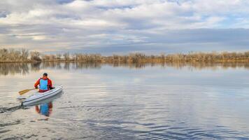 anziano maschio paddler è paddling un' addobbato spedizione canoa su un' calma lago nel settentrionale Colorado, inverno scenario senza neve foto