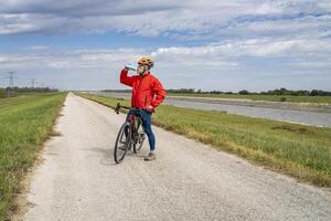 anziano atletico uomo è potabile acqua durante bike un' ghiaia turismo bicicletta su un' argine pista lungo catena di rocce canale vicino granito città nel Illinois foto