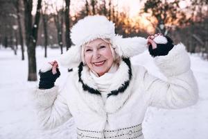 donna anziana in cappello bianco e pelliccia che si gode l'inverno nella foresta di neve. inverno, età, concetto di stagione foto