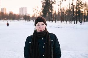 donna anziana in cappello e giacca sportiva che fa esercizi sportivi nel parco invernale di neve. inverno, età, sport, attività, concetto di stagione foto