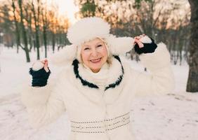 donna anziana in cappello bianco e pelliccia che si gode l'inverno nella foresta di neve. inverno, età, concetto di stagione foto