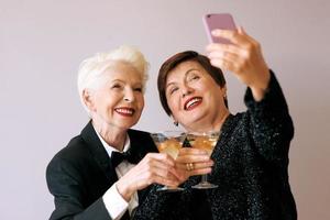 due belle donne anziane mature alla moda che bevono vino e fanno foto selfie. divertimento, festa, tecnologia, stile, concetto di celebrazione