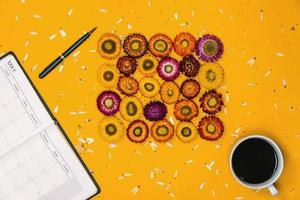 vista dall'alto concetto di sfondo giallo pastello. fiori colorati che sono disposti in forma con una penna per taccuino e una tazza di caffè posizionati. foto