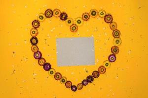 vista dall'alto concetto di sfondo giallo pastello, fiori colorati disposti a forma di cuore. cartolina di concetto. foto