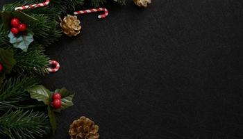 vista dall'alto decorazioni natalizie, foglie di abete di pino, bastoncino di zucchero e bacche rosse su sfondo nero scuro strutturato foto