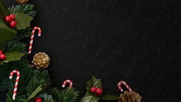 vista dall'alto decorazioni natalizie, foglie di abete di pino, bastoncino di zucchero e bacche rosse su sfondo nero scuro strutturato foto
